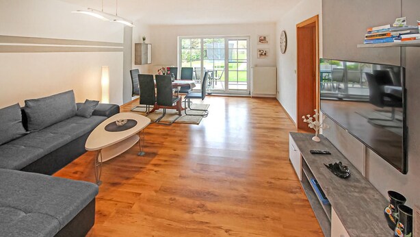 Ein modernes Wohnzimmer mit grauem Sofa, Couchtisch und Fernseher auf einem Standfuß.