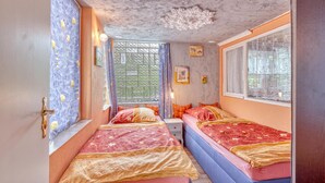 A room with two beds, a window with a view, a decorative ceiling, and a door with a handle. - Ferienhaus Fürstenberg/Havel (Fürstenberg/Havel OT H)