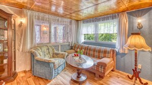 A cozy room with a wooden ceiling, a blue armchair, a plaid sofa, a round table, and a lamp. - Ferienhaus Fürstenberg/Havel (Fürstenberg/Havel OT H)