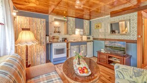 A cozy living room with a wooden ceiling, a dining table with apples, a sofa, and a kitchen area with a stove and microwave. - Ferienhaus Fürstenberg/Havel (Fürstenberg/Havel OT H)