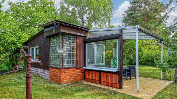 A rustic wooden house with a glass conservatory, a brick foundation, and a metal water spigot. - Ferienhaus Fürstenberg/Havel (Fürstenberg/Havel OT H)