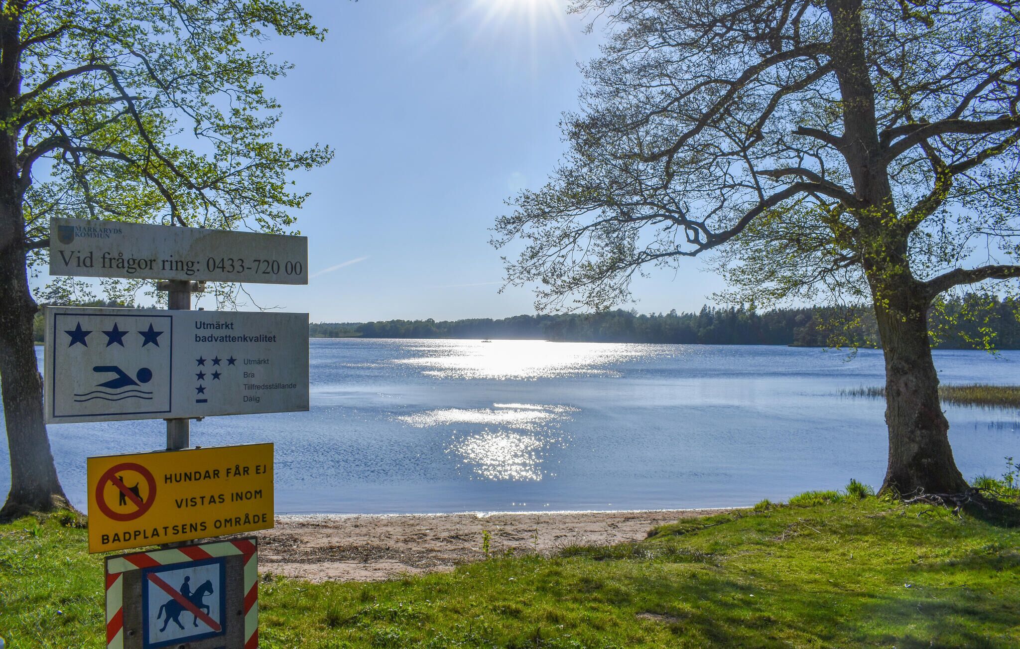 Uitzicht op een meer met borden die zwemgebieden en beperkingen aangeven.