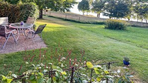 A patio with outdoor furniture and a table, surrounded by a well-maintained lawn and garden.
