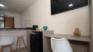 A modern kitchen with a flat-screen TV, two white chairs, a black refrigerator, and a small ship decoration on the counter. - Solaris Serrambi Flats (Ipojuca)