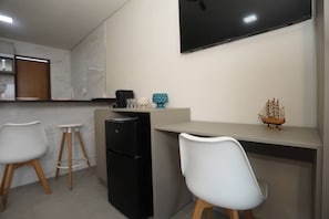 A modern kitchen with a flat-screen TV, two white chairs, a black refrigerator, and a small ship decoration on the counter. - Solaris Serrambi Flats (Ipojuca)