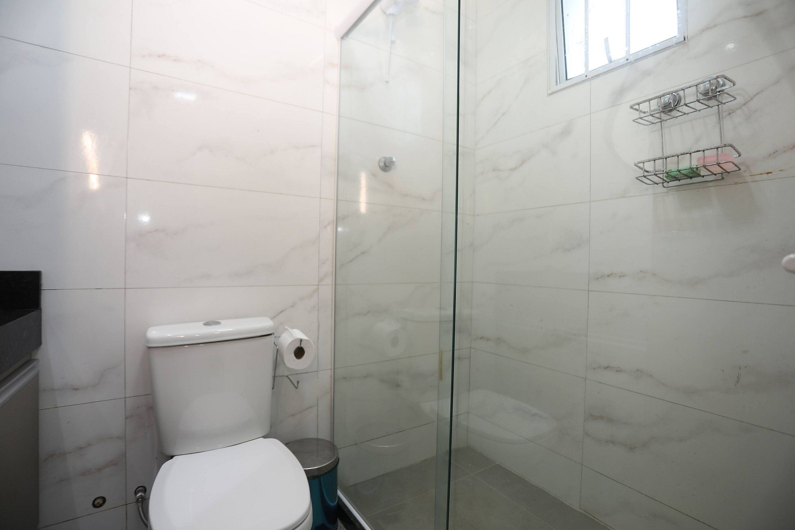 Une salle de bain équipée de toilettes, d’une douche à parois de verre et d’un mur recouvert de carreaux de marbre.