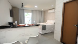 A hotel room with a bed, a desk with a chair, a TV, and a door. - Solaris Serrambi Flats (Ipojuca)