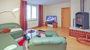 A living room with green sofas, a glass coffee table, a television, and a wood-burning stove. - Ferienwohnung Ostseebad Breege (Ostseebad Breege OT Ju)
