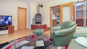 A living room with a sofa, a glass coffee table, a television, a fireplace, and a kitchen area visible through an open door. - Ferienwohnung Ostseebad Breege (Ostseebad Breege OT Ju)