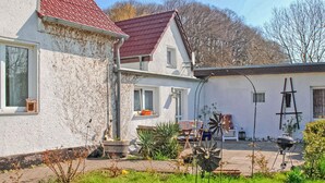 A two-story house with a red roof, a garden with various plants, and a barbecue grill. - Ferienwohnung Ostseebad Breege (Ostseebad Breege OT Ju)