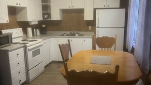 Une cuisine de taille réduite avec des meubles blancs, une table à manger en bois et un réfrigérateur.