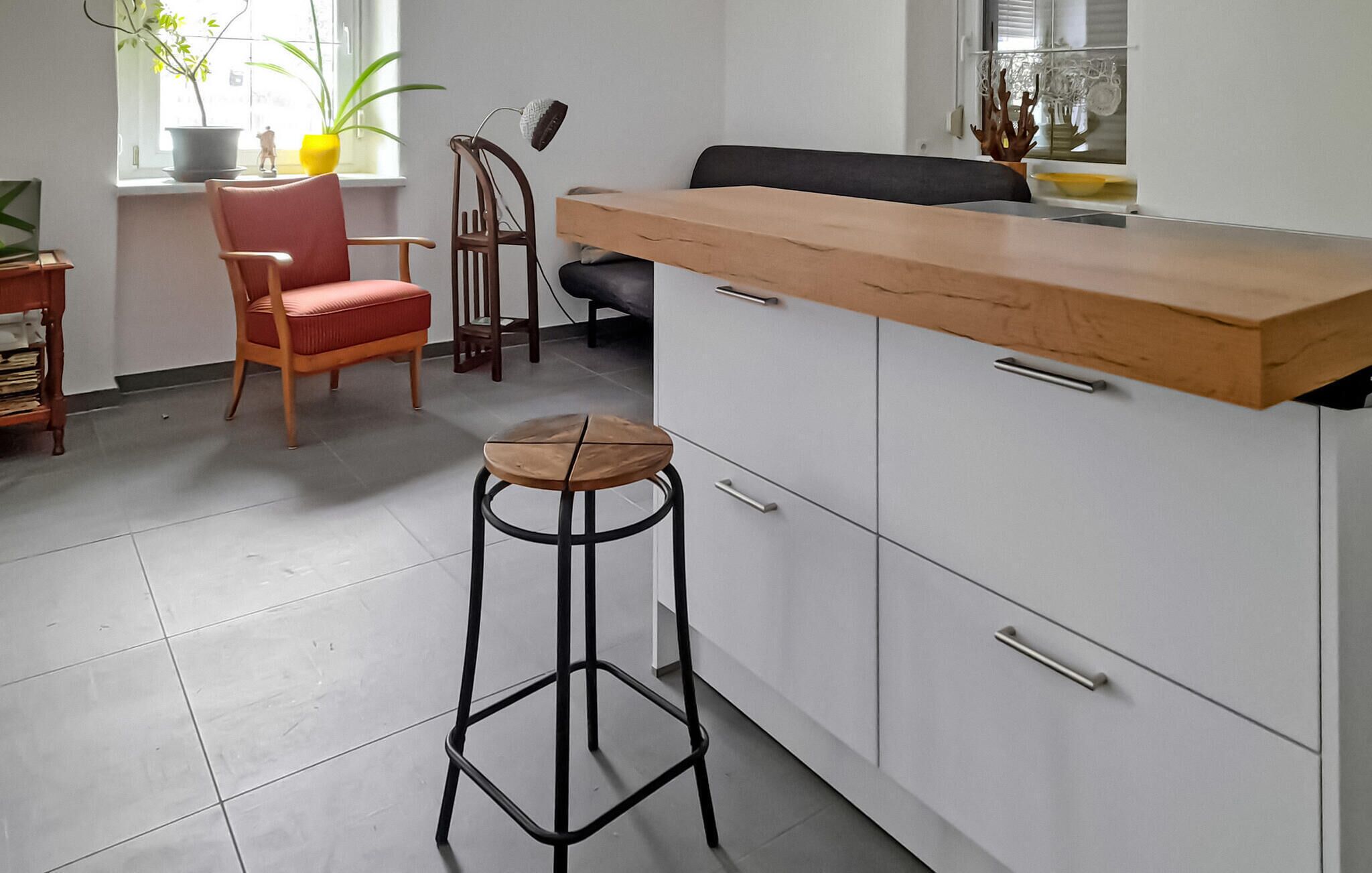 Una cocina con encimera de madera, una silla roja, un taburete y una ventana con plantas.