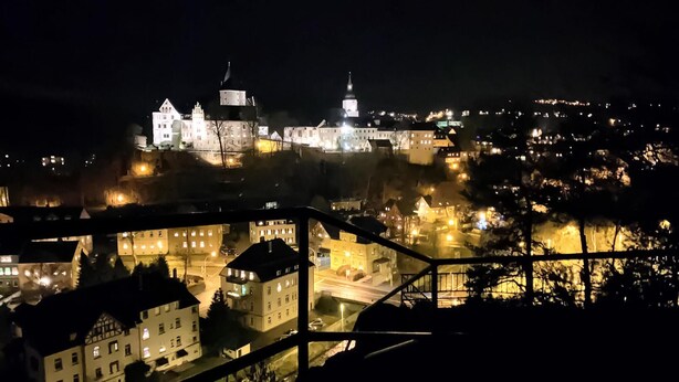 A nighttime view of a historic castle with illuminated towers and a prominent dome, surrounded by a town with lit buildings and a bridge. - Ferienwohnung Schwarzenberg (Schwarzenberg)
