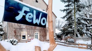 A building with a sign that reads "Fewo" in front of a wooden fence and snow-covered trees. - Ferienwohnung Schwarzenberg (Schwarzenberg)