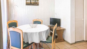 Un coin repas comprenant une table ronde, quatre chaises, une petite table d’appoint en bois sur laquelle se trouve un téléviseur, et un tableau accroché au mur.