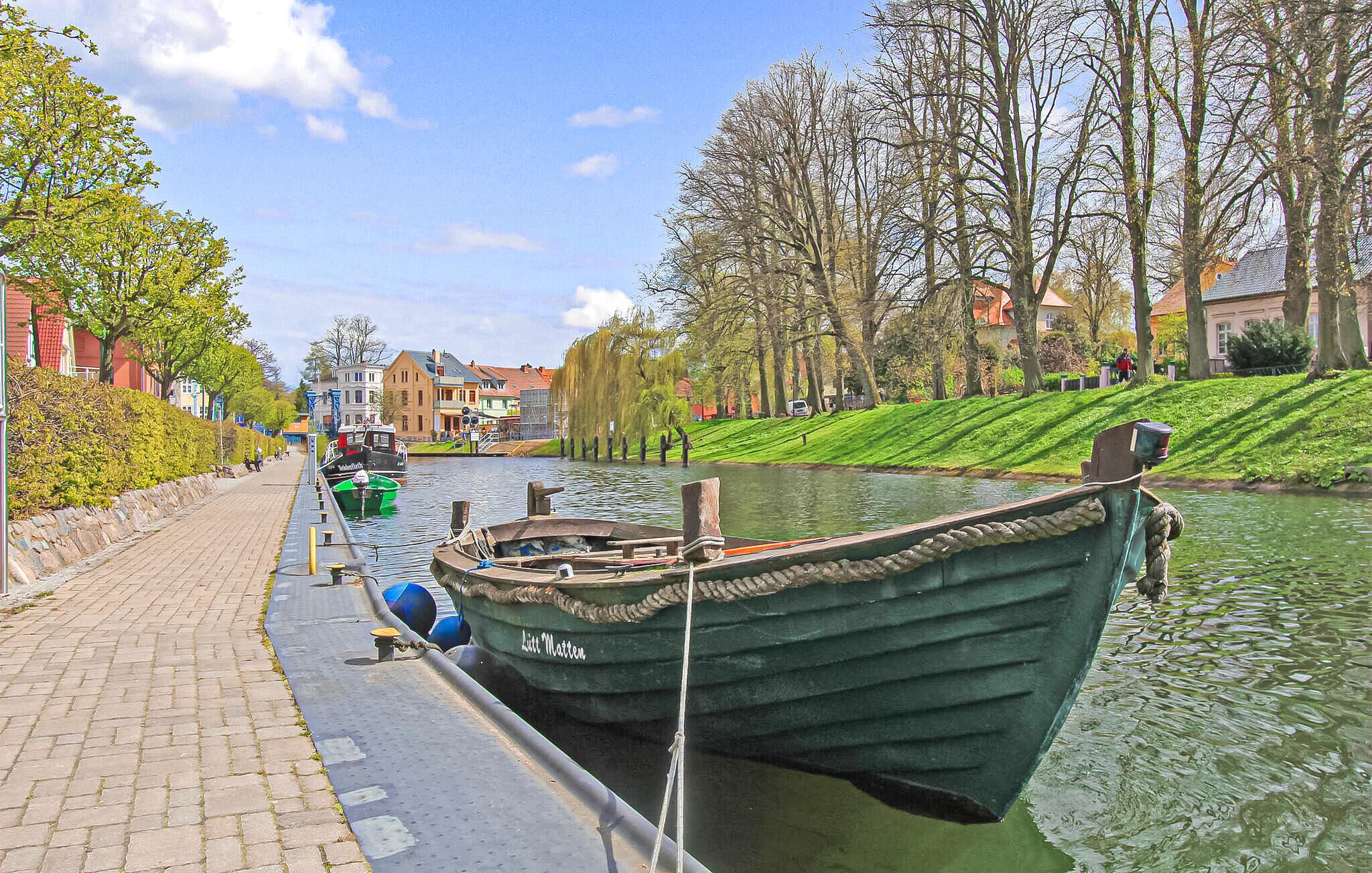 Un canal bordé d’arbres et de bâtiments, avec une barque à rames amarrée au bord.
