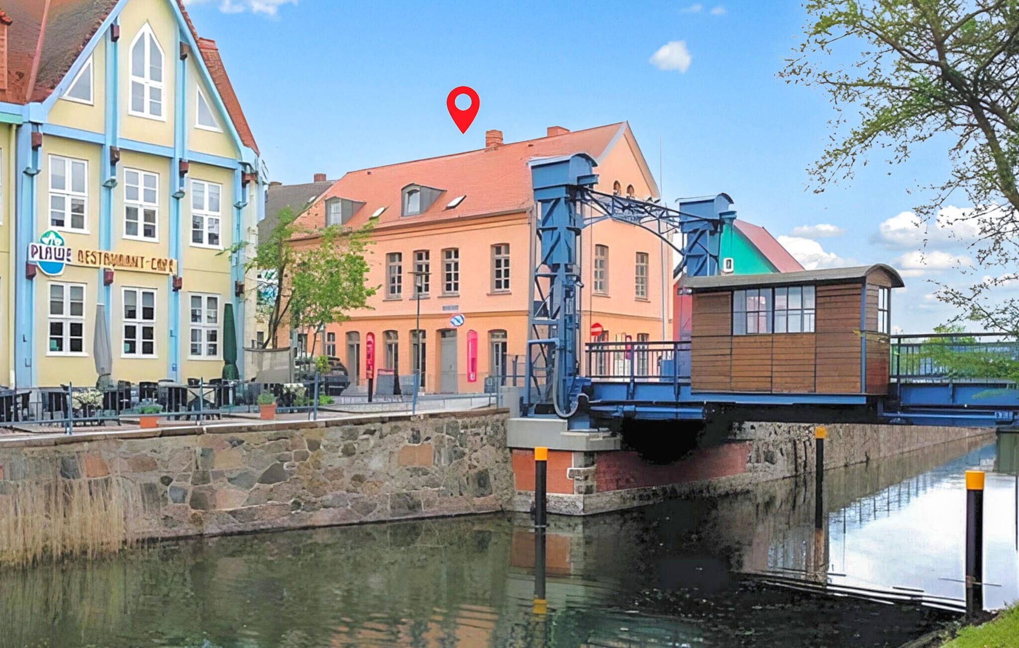 Un canal surmonté d’un pont, un restaurant appelé « Plage Destroyant Cafe » sur la gauche, et un bâtiment avec un toit rouge au centre.