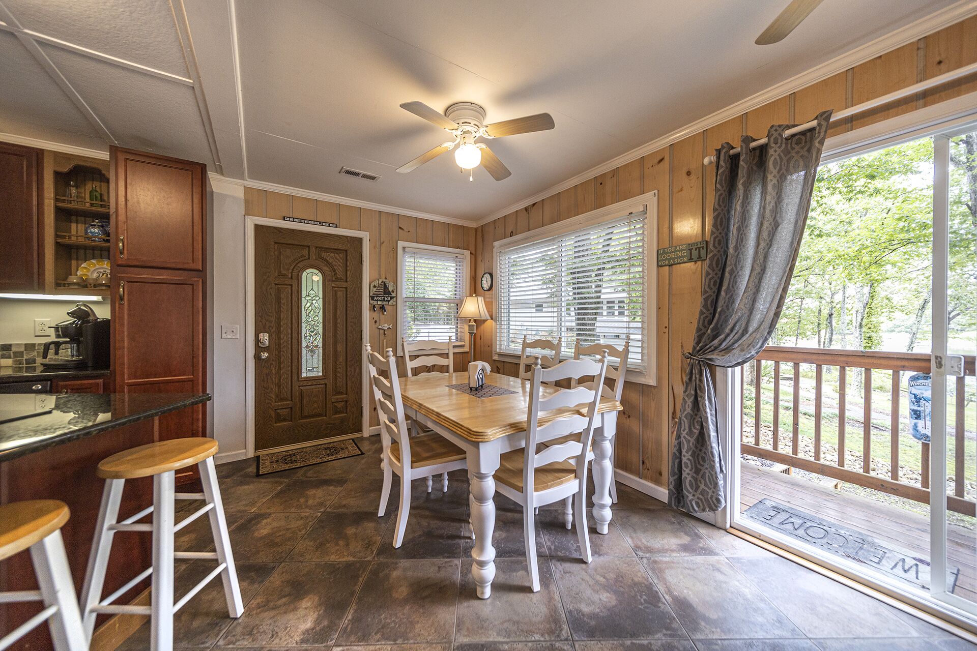 A kitchen with a dining area, wooden walls, a ceiling fan, and a view of the outdoors.