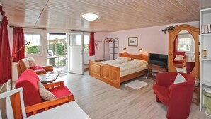Ein gemütliches Zimmer mit Bett, Fernseher, Sessel und Tisch.