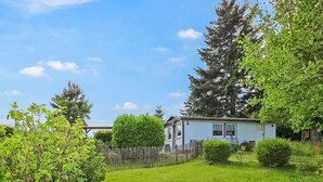 Ein kleines, eingeschossiges Haus mit umzäunter Garten, umgeben von Bäumen und Grünpflanzen.