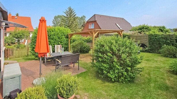 Ein Garten mit Terrassentisch und -stühlen, einer Holzpergola und einem gepflegten Rasen.