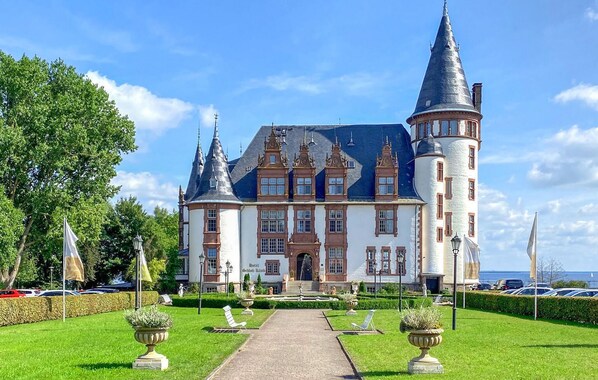 Een groot, historisch gebouw met meerdere torens en een centrale ingang, omgeven door goed onderhouden tuinen en paden.