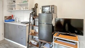 Une cuisine compacte équipée d’un réfrigérateur, d’un four à micro-ondes, d’une machine à café et d’un petit téléviseur posé sur un meuble en bois.