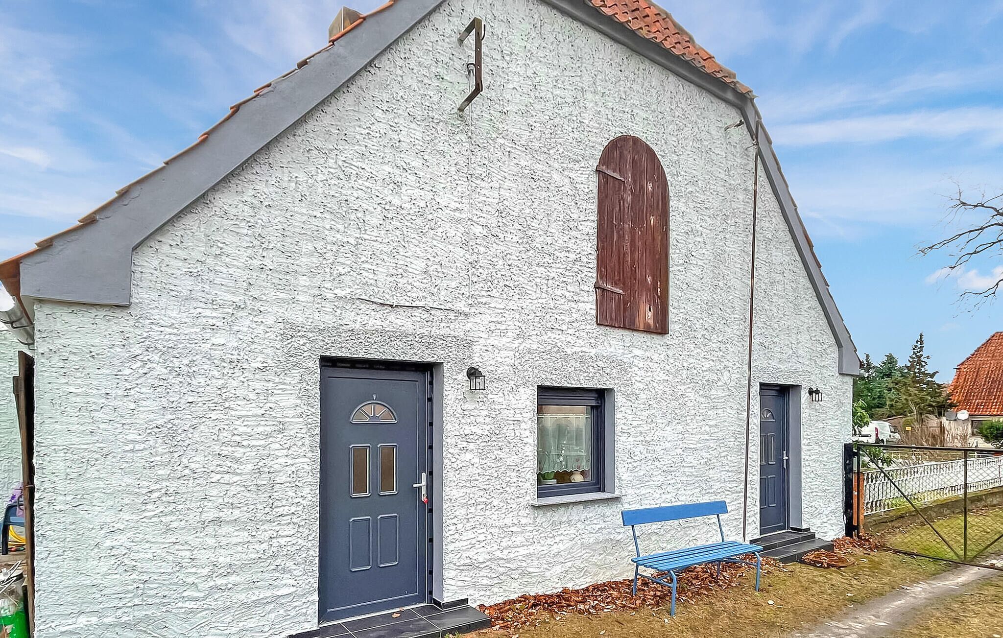 Un bâtiment blanc avec une porte sombre, une petite fenêtre et un banc bleu à l’extérieur.