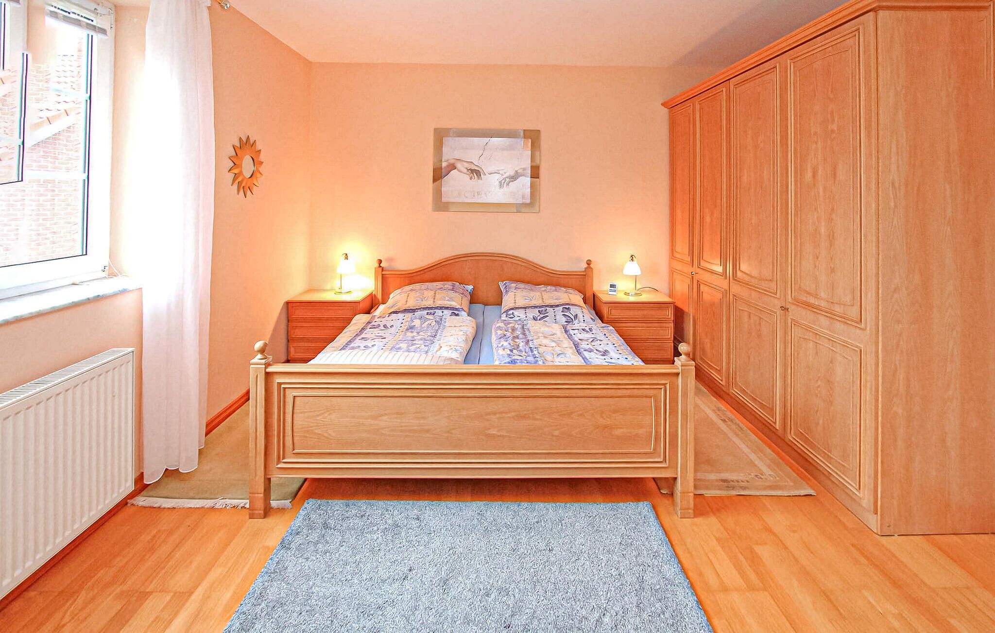 Ein Schlafzimmer mit einem hölzernen Bett, zwei Nachttischen mit Lampen, einem großen Kleiderschrank, einem gerahmten Kunstwerk an der Wand und einem Fenster mit Vorhängen.