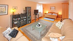 A cozy living room with a sofa, a coffee table, and a TV. There's a cabinet with glass doors and a bed with a wooden headboard.