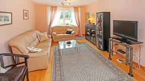 A living room with a beige sofa, a glass coffee table, a TV on a stand, and a cabinet with glass doors.