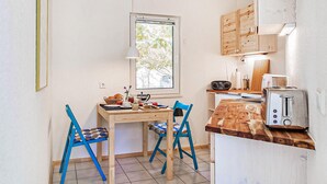 A small kitchen with a wooden table, two blue chairs, a window, and basic appliances. - Ferienwohnung Rheinsberg (Rheinsberg OT Kagar)