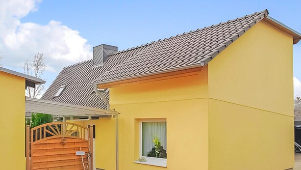 Ein gelbes Gebäude mit einem Ziegeldach, einem hölzernen Tor und einem kleinen Fenster mit einer Pflanze.