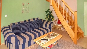 Ein Wohnzimmer mit einem gestreiften Sofa, einer Holztreppe und einem kleinen Tisch mit einem Gesellschaftsspiel.