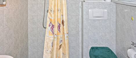 A bathroom with a shower curtain, a toilet, and a towel rack with towels.