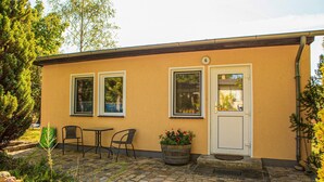 A building with a beige exterior, two windows, a door, and a small patio area with a table and chairs.