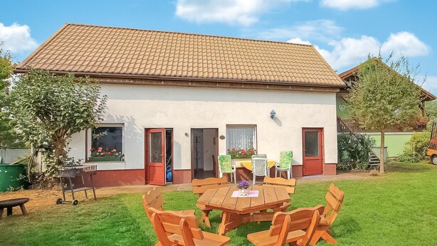 A two-story house with a tiled roof, a front porch with wooden chairs, and a small garden. - 1 bedroom beautiful home in Luckow (Luckow)