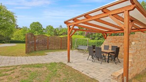 Un espace extérieur aménagé en terrasse, avec une pergola, une table et des chaises, et un mur en briques.