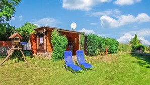 A rustic wooden cabin with a satellite dish, two blue lawn chairs, and a small garden area.