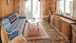 A cozy cabin interior with a plaid sofa, wicker chairs, a small table, and wooden cabinets.