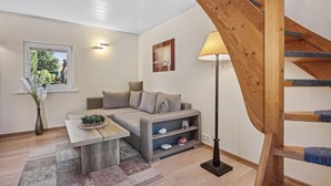Ein modernes Wohnzimmer mit einem grauen Sofa, einem Holztisch, einer Stehlampe und einer Treppe mit Holzhandlauf.