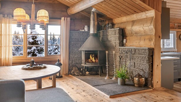 A cozy cabin interior with a stone fireplace, wooden beams, and a view of snow-covered trees. - Stunning home in Gol with sauna (Gol)