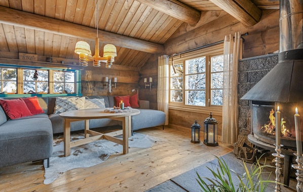 A log cabin interior with a sofa, table, fireplace, and windows with a snowy view.