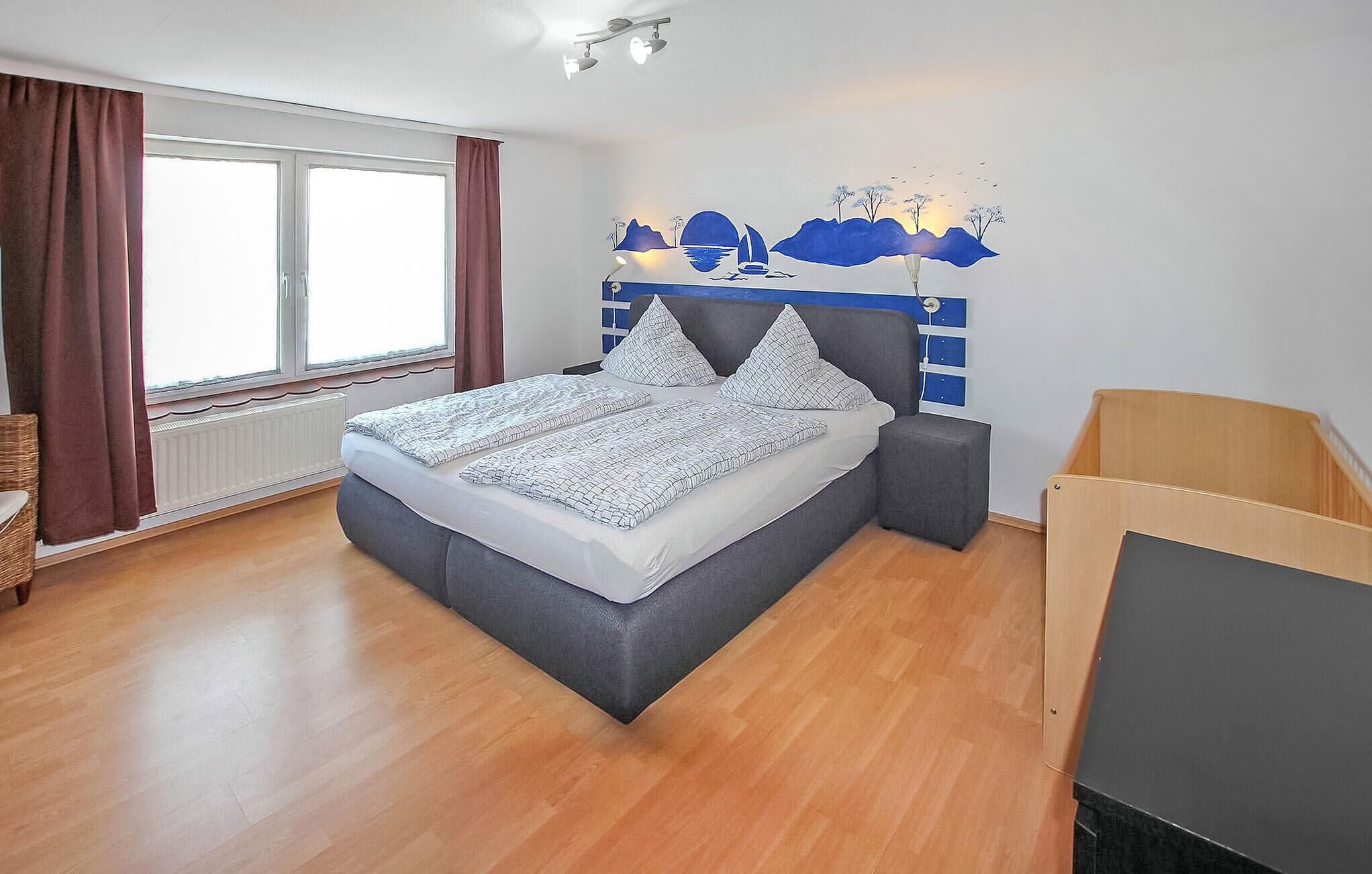 Une chambre à coucher avec un lit, une fenêtre avec des rideaux, un luminaire fixé au mur et un plancher en bois.