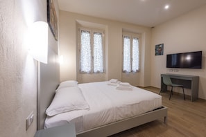 Une chambre à coucher avec un lit, un bureau, une chaise, un téléviseur et des fenêtres avec des rideaux.