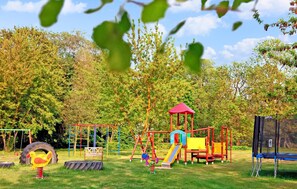 Explore the park's playground, featuring a slide, swings, and climbing frame amidst lush greenery and trees.