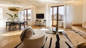 A modern living room with a sofa, ottoman, dining table, chairs, and a TV. - Oro1 Florence Luxury Apartment by Mmega (Firenze)