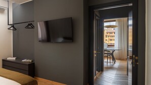 A modern hotel room with a bed, a TV mounted on the wall, a dark door, and a view of the outside. - Oro1 Florence Luxury Apartment by Mmega (Firenze)
