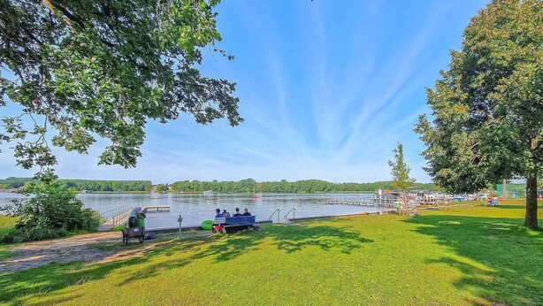 A lakeside park with a grassy area, a dock, and a boat. - Doppelhaushälfte Mirow Starsow (Mirow OT Starsow)