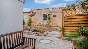 A courtyard with a wooden bench, a stone pathway, and a rustic building with a satellite dish. - 2 bedroom amazing home in Altwarp (Altwarp)